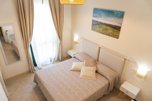 A hotel room with a bed, bedside tables, a mirror, and a painting on the wall.