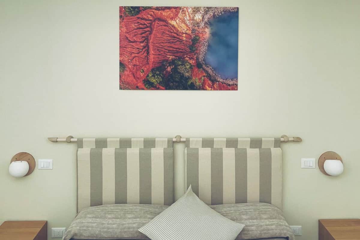 Un dormitorio con una cama, cabecera, lámpara colgante, un cuadro en la pared y mesitas de noche.