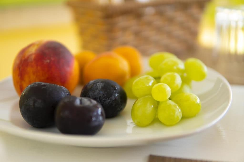 Un plato con frutas, entre ellas un melocotón, uvas y ciruelas.