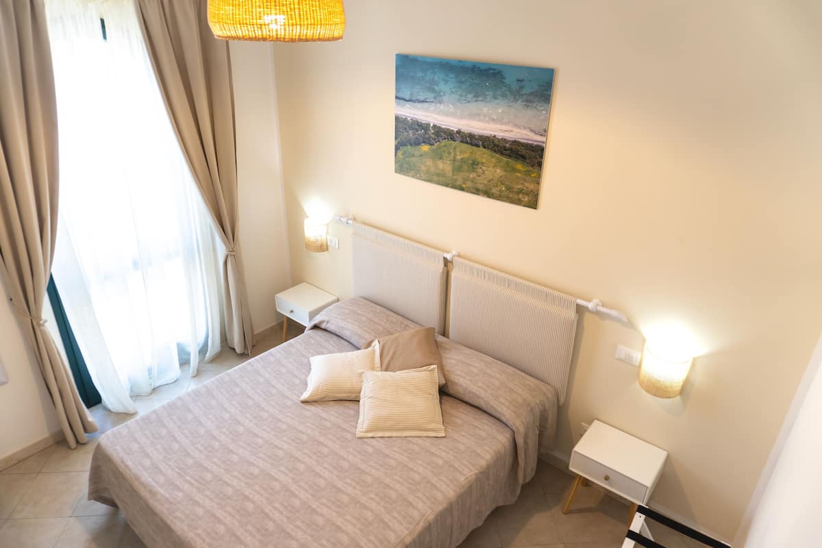 Un dormitorio ordenado con una cama, mesitas de noche, un cuadro y una lámpara.