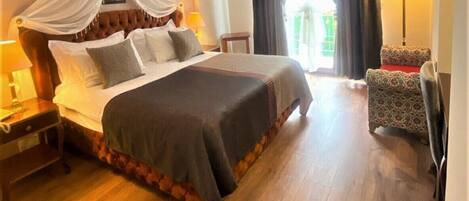 Quarto de hotel com uma cama grande, mesa de cabeceira, cadeira e televisão.