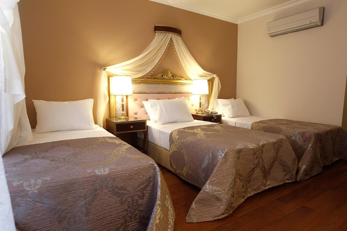 A hotel room with two beds, a canopy bed, and a nightstand with a lamp.