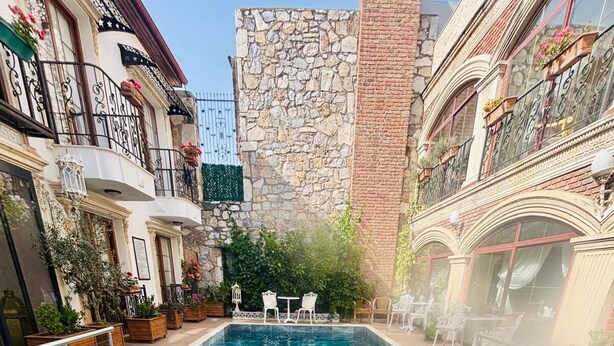 Zona de piscina con muro de piedra, asientos exteriores y una persona sentada junto a la piscina.
