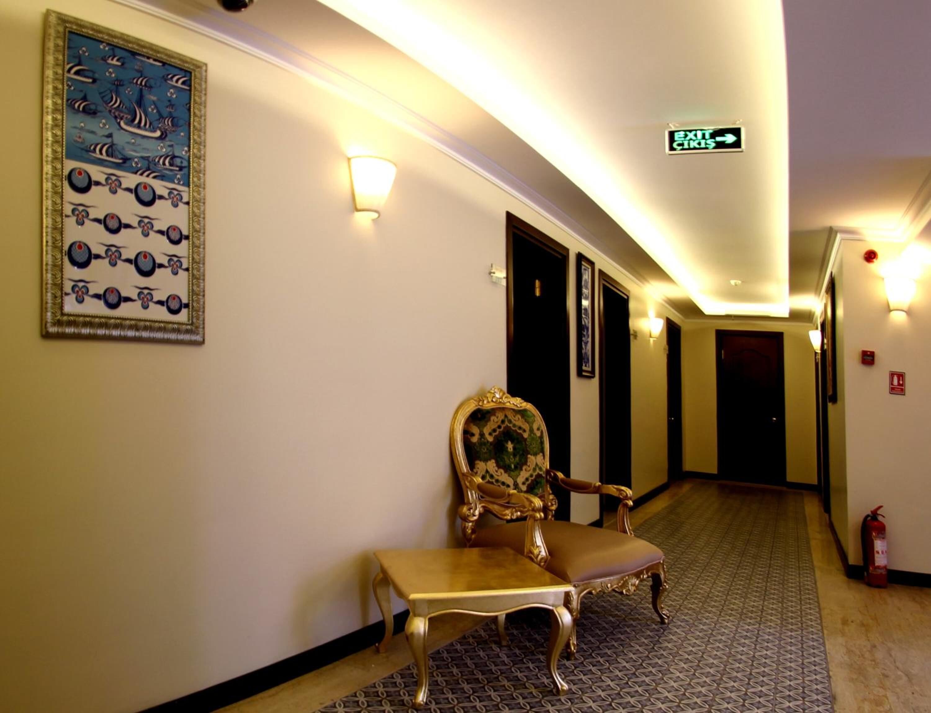 A hotel hallway with a bench, framed artwork, exit signs, and a fire extinguisher.