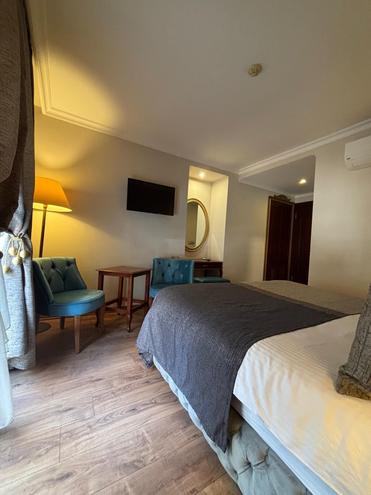 A hotel room with a bed, a desk, two chairs, a TV, a mirror, and a wardrobe.