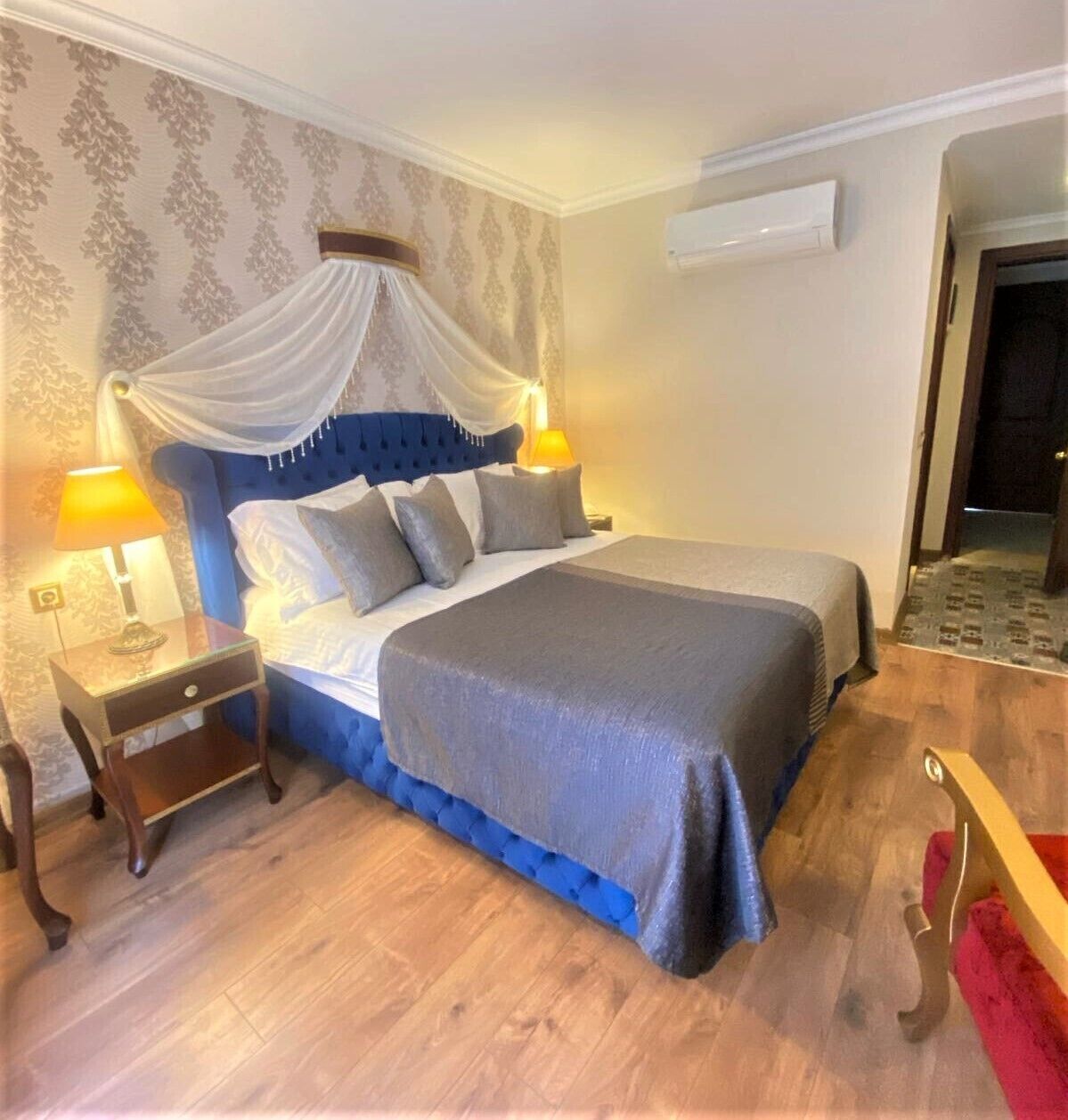 A bedroom with a bed, nightstands, a canopy, and an air conditioning unit.