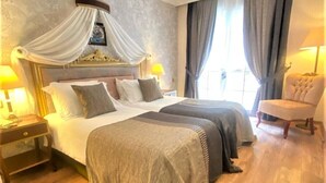 Habitación de hotel con dos camas, una cama con dosel, un área de descanso con una silla y un ventanal con cortinas.