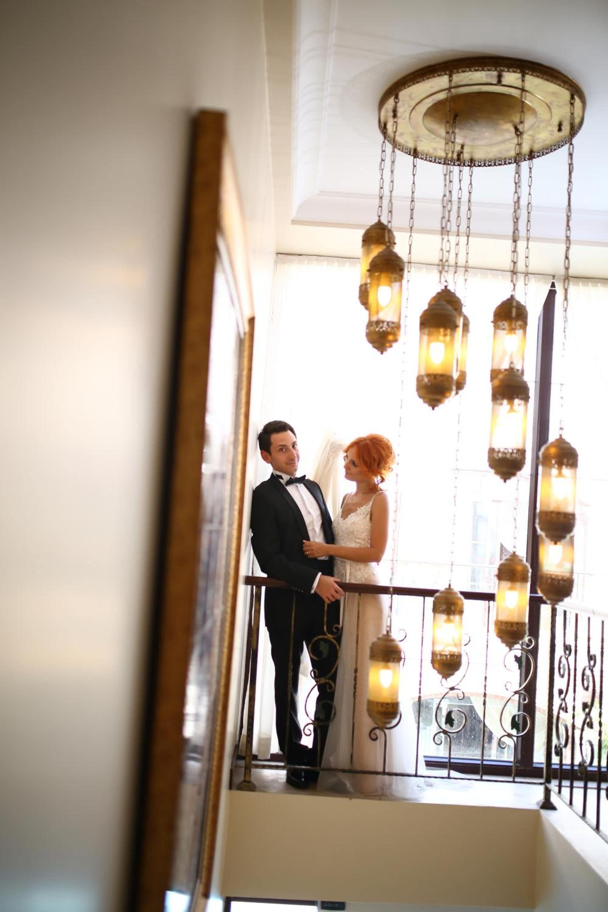 A couple on a balcony with hanging lanterns, a railing, and a view of the city.