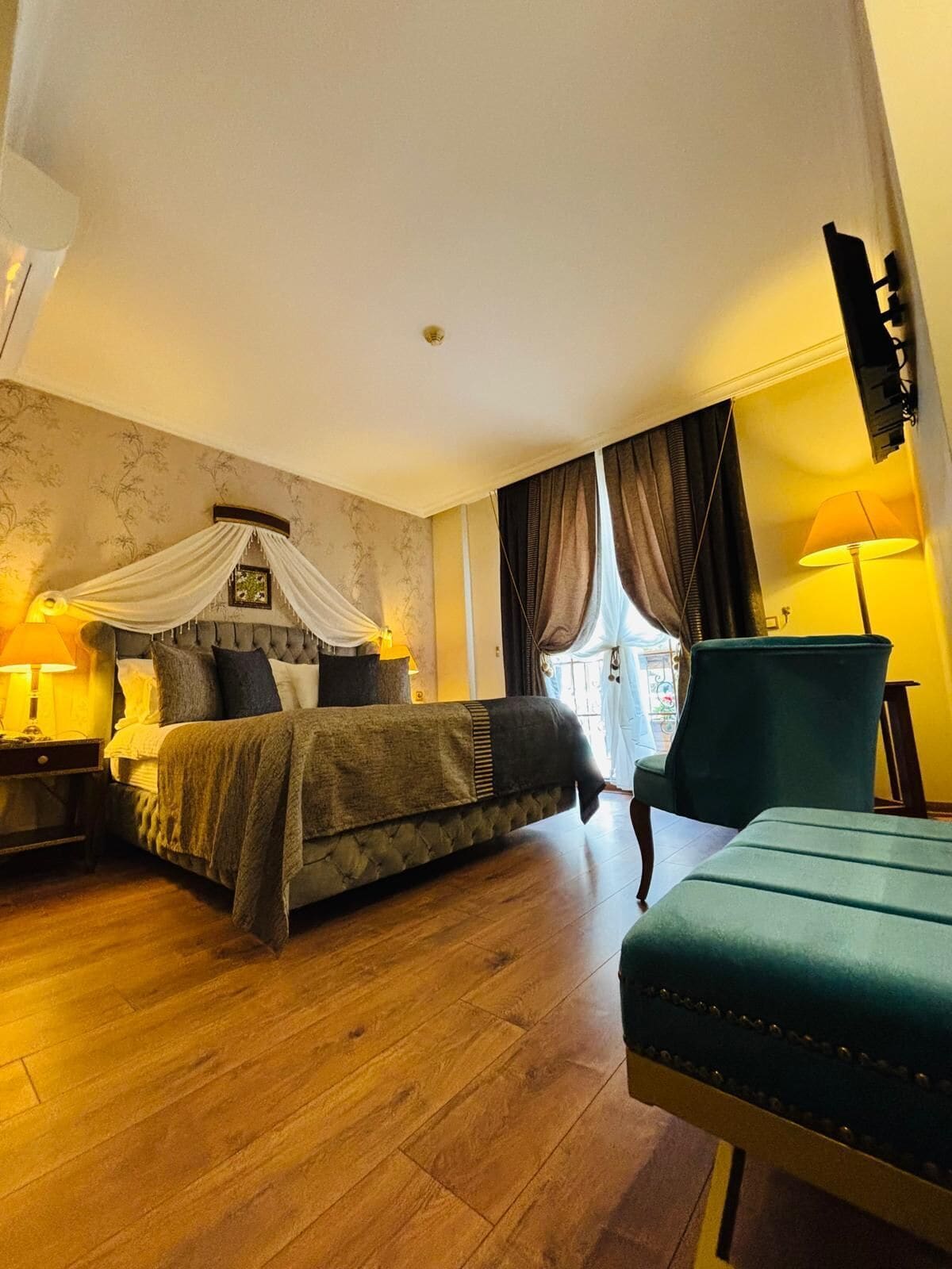 Un dormitorio con cama, mesita de noche, silla, ventana con cortinas y lámpara.
