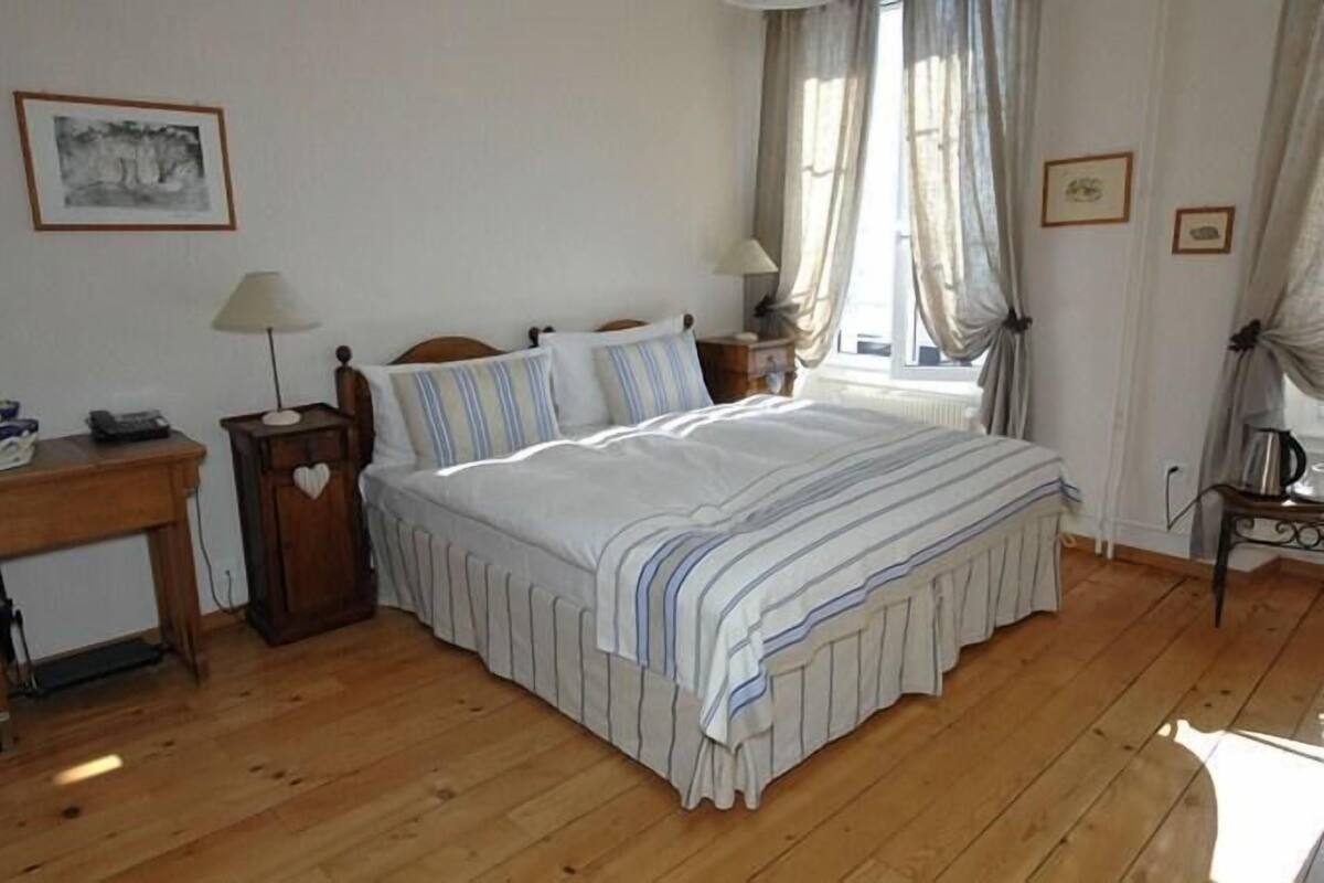 Un dormitorio con cama, mesitas de noche, escritorio y ventana con cortinas.