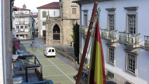 A historic building with a bell tower, a flag, and a street with parked cars. - Albergaria da Sé (Braga)
