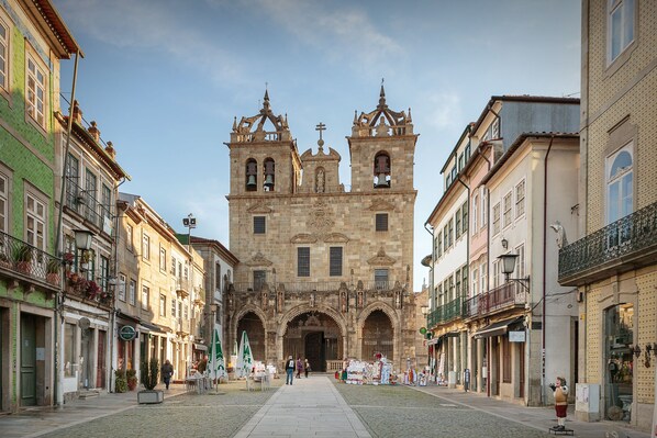 A historic building with a prominent entrance and two towers, surrounded by traditional buildings with balconies and shops.