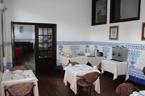 Zona pranzo con tavoli apparecchiati, sedie e angolo cottura sullo sfondo.