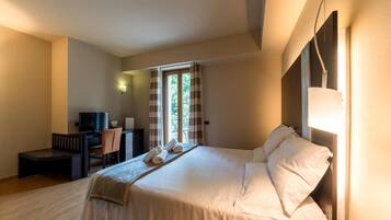 A hotel room with a bed, a desk with a chair, a television, and a window with curtains.