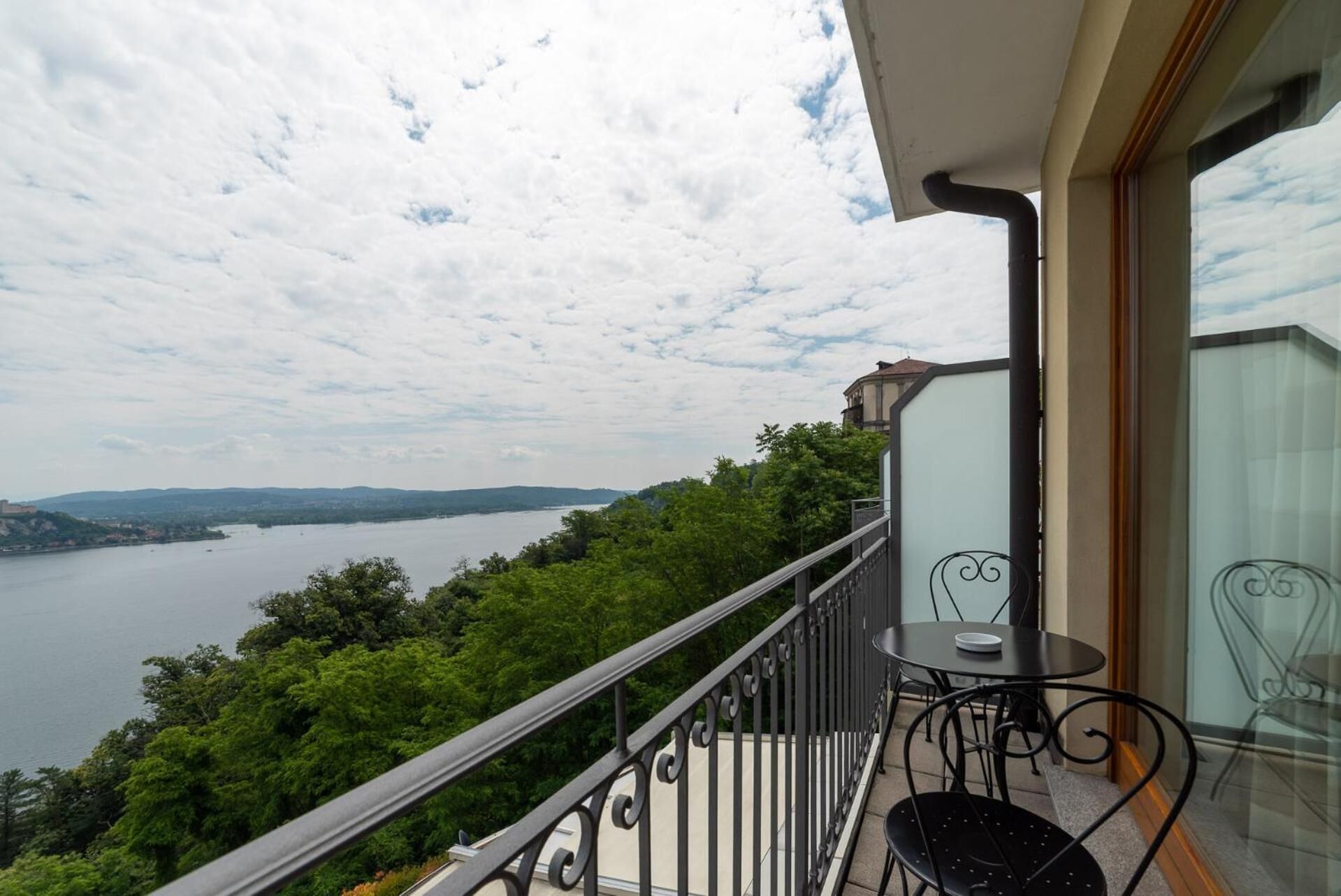 A balcony with a view of a lake and hills, a table with chairs, and a glass door.