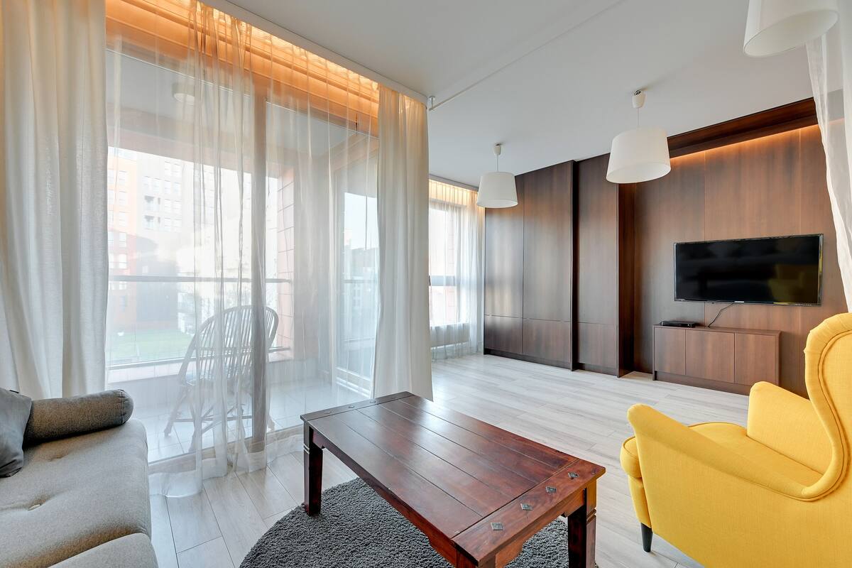 A modern living room with a sofa, yellow armchair, wooden coffee table, and a TV mounted on the wall.