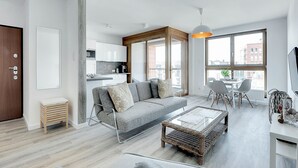 A modern living room with a grey sofa, a coffee table, and a dining area with chairs and a table. - Apartinfo Aura Apartments (Gdansk)