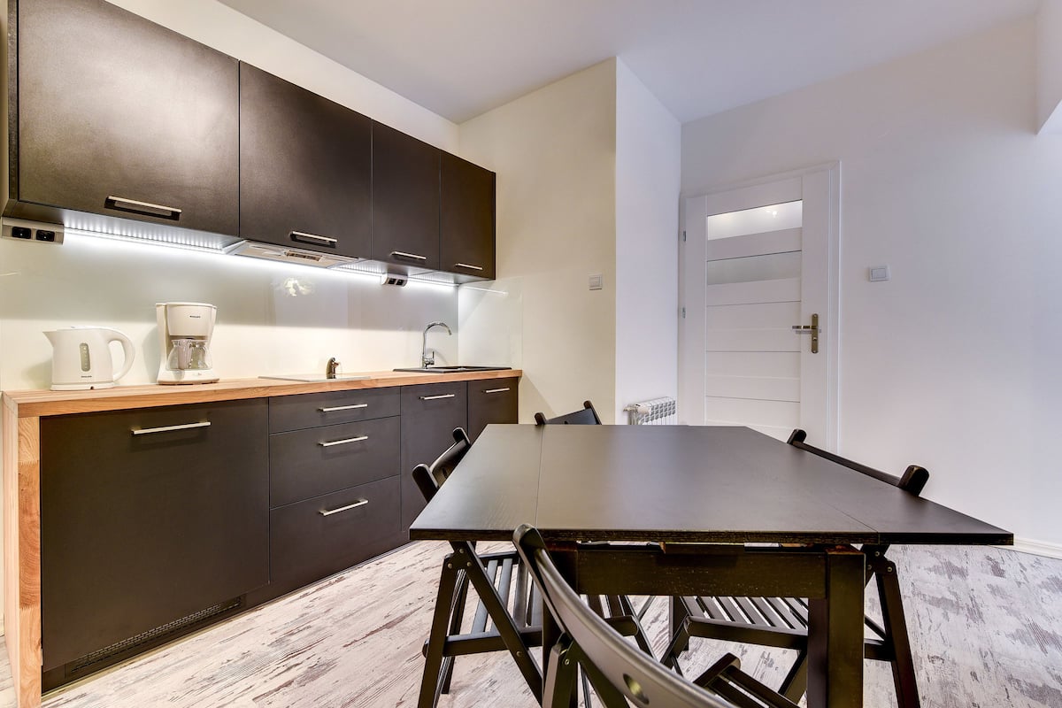 A modern kitchen with dark cabinets, a wooden countertop, and a large dining table.