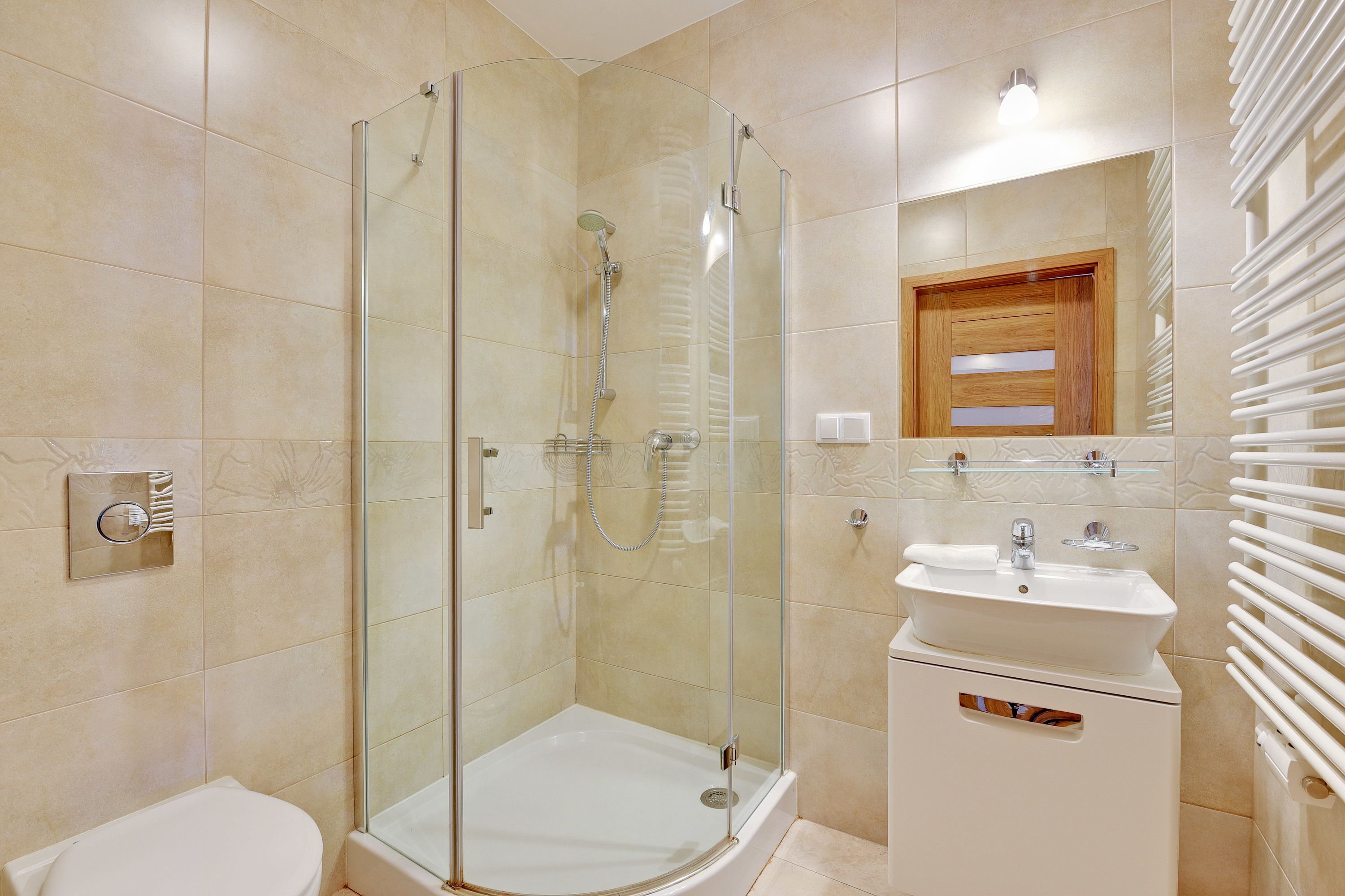 Un baño moderno con ducha envuelta en vidrio, un lavamanos blanco y un armario de medicinas de madera.
