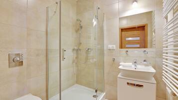 Un baño moderno con ducha envuelta en vidrio, un lavamanos blanco y un armario de medicinas de madera.