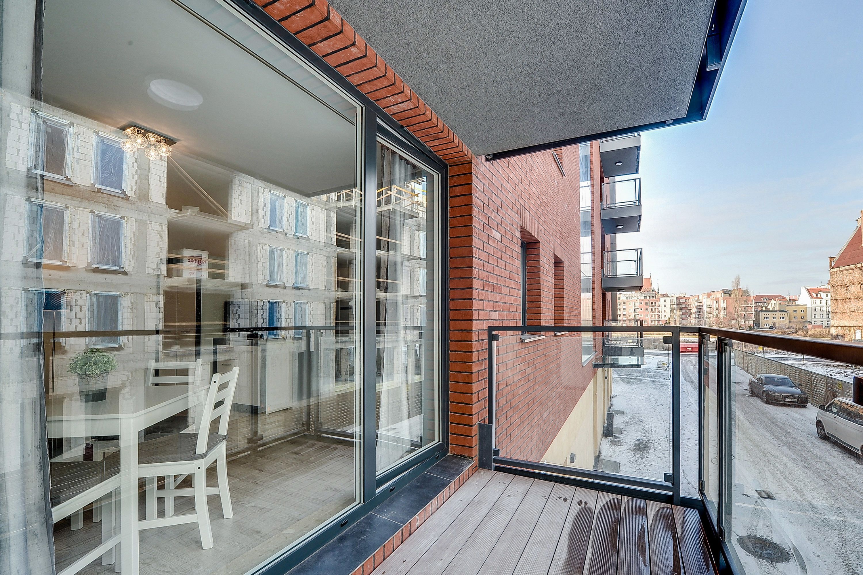 Un balcon avec une porte vitrée donnant sur une pièce comprenant une table et des chaises, un mur en briques et une vue sur la rue.