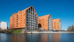 A modern building with a unique architectural design, featuring a prominent sloped roof and a reflective glass facade. - Apartinfo Aura Apartments (Gdansk)
