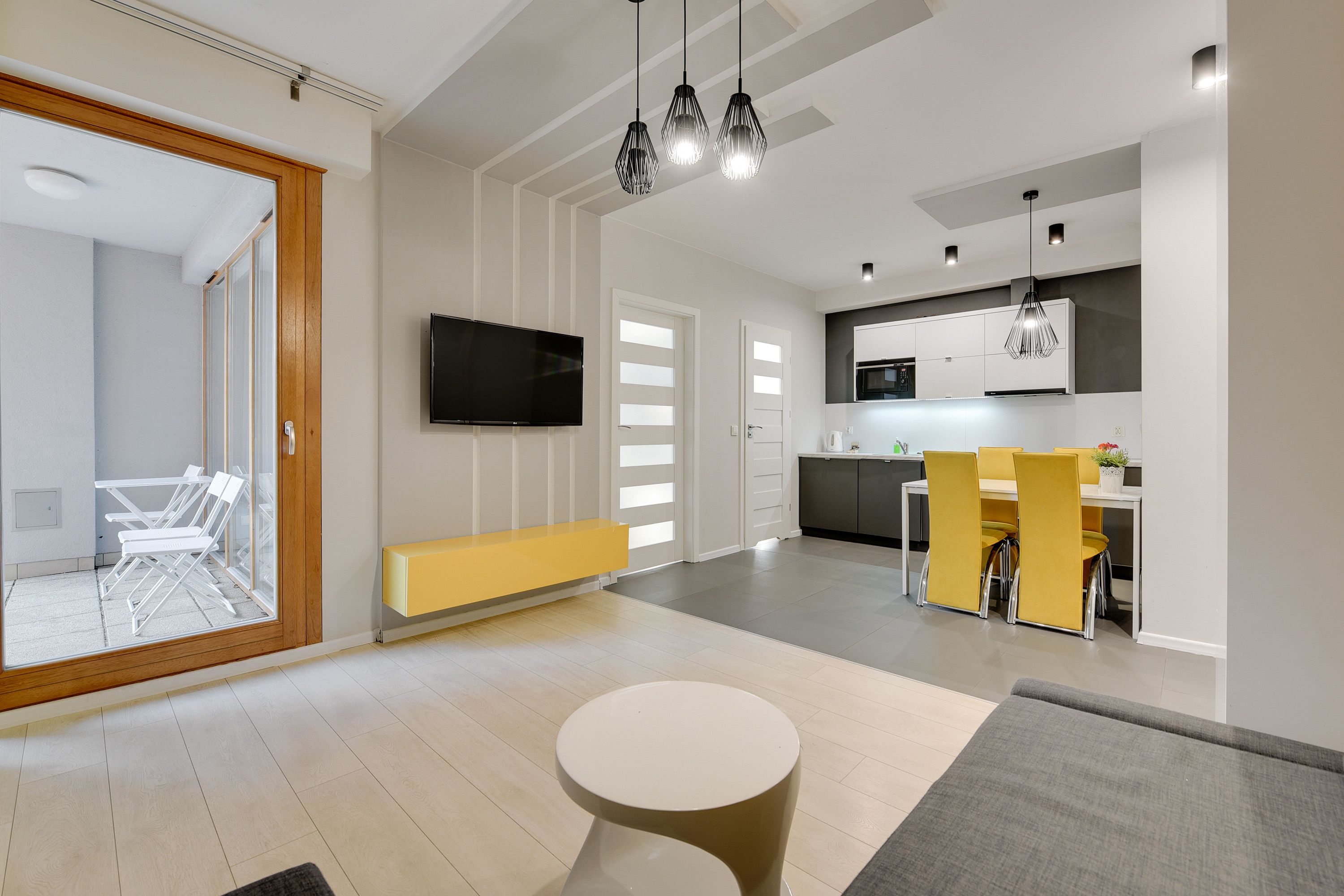A modern living room with a sofa, a coffee table, and a dining area with yellow chairs.