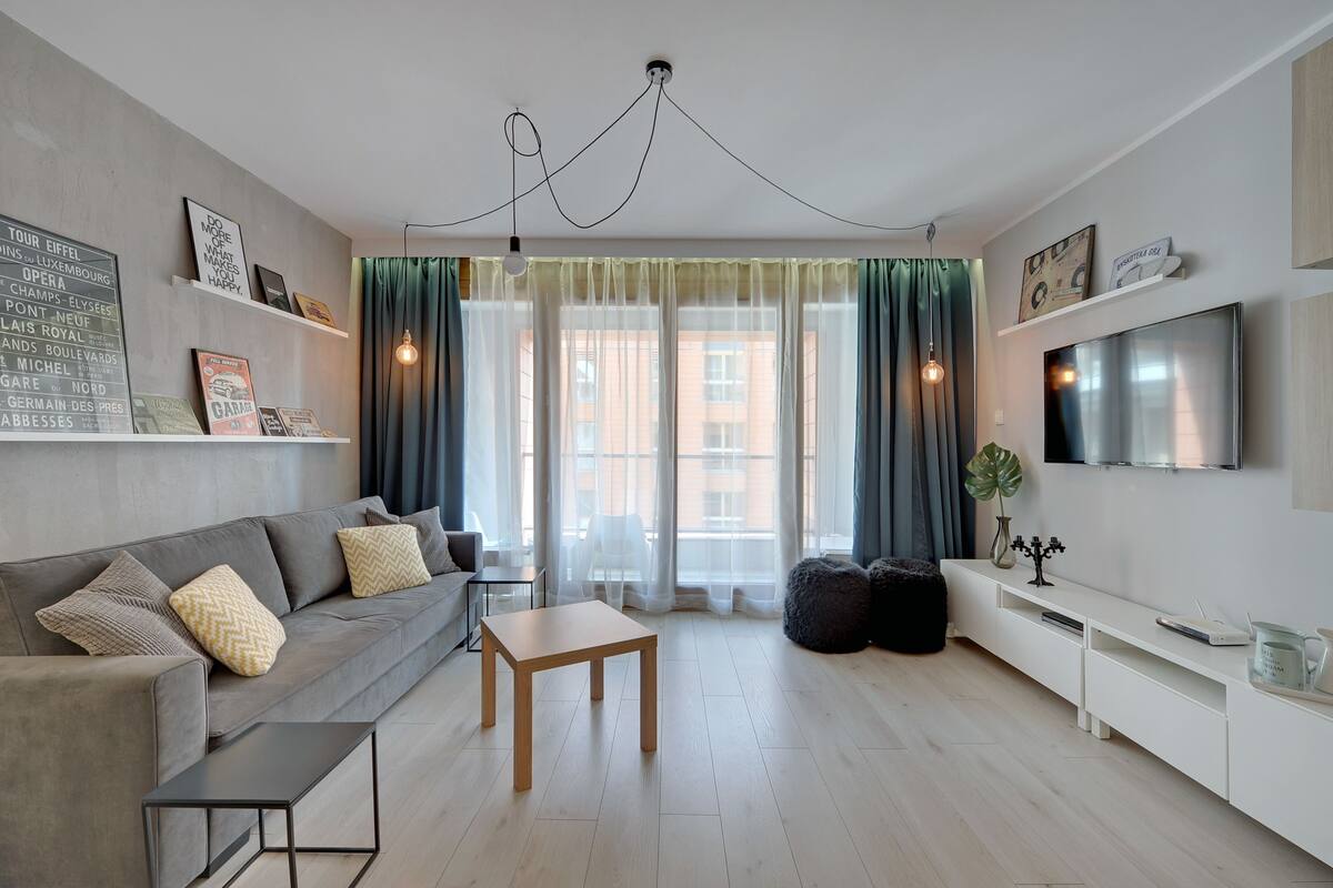 A modern living room with a grey sofa, wooden coffee table, and a TV on a white stand.