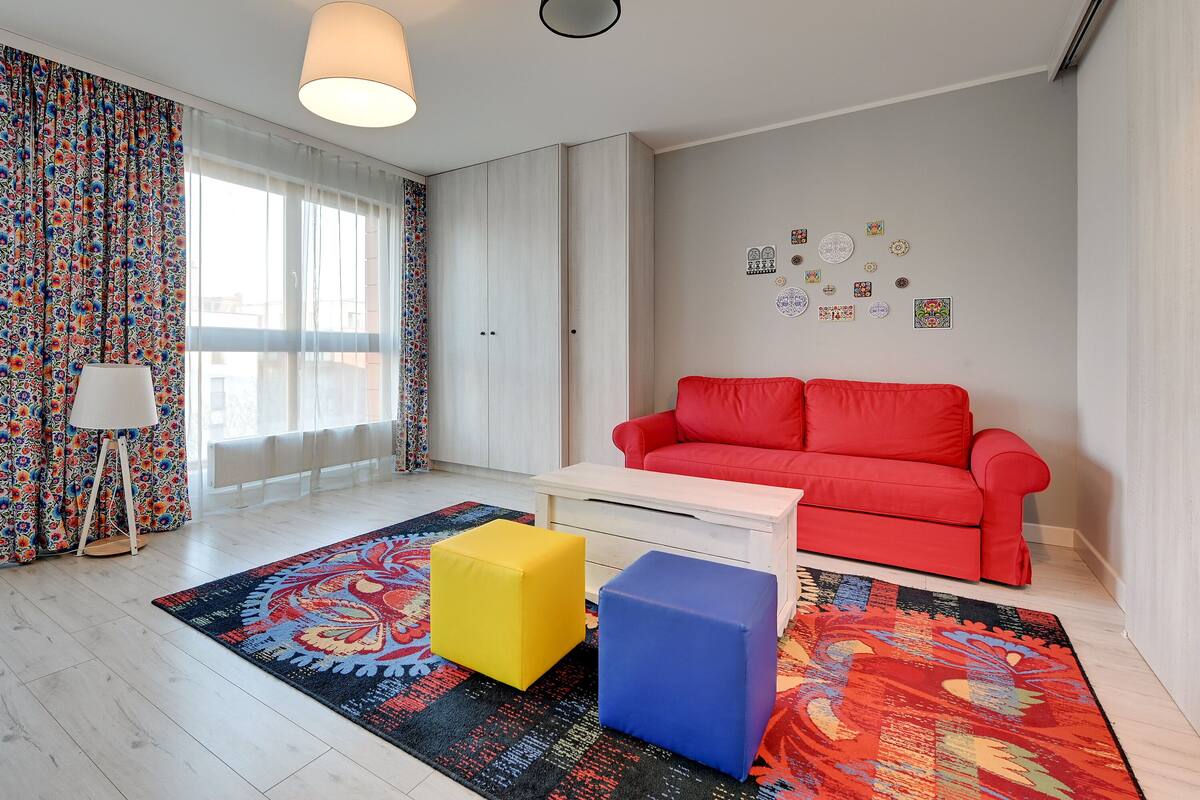 A modern living room with a red sofa, a white coffee table, and colorful ottomans.