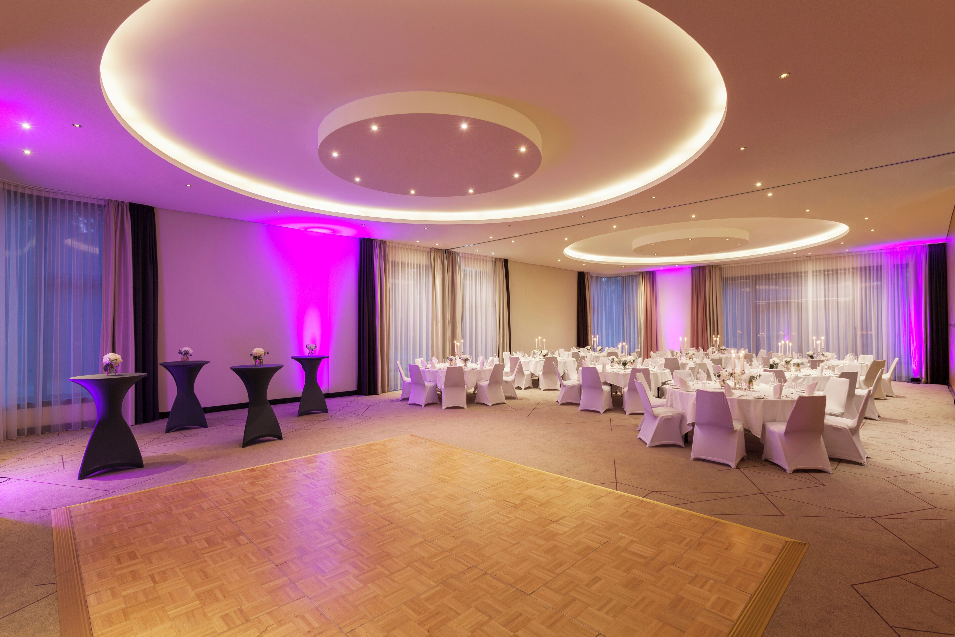 Un amplio salón de banquetes con mesas y sillas redondas, una pista de baile e iluminación ambiental.