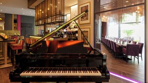 A grand piano in a spacious room with a bar area and dining space.