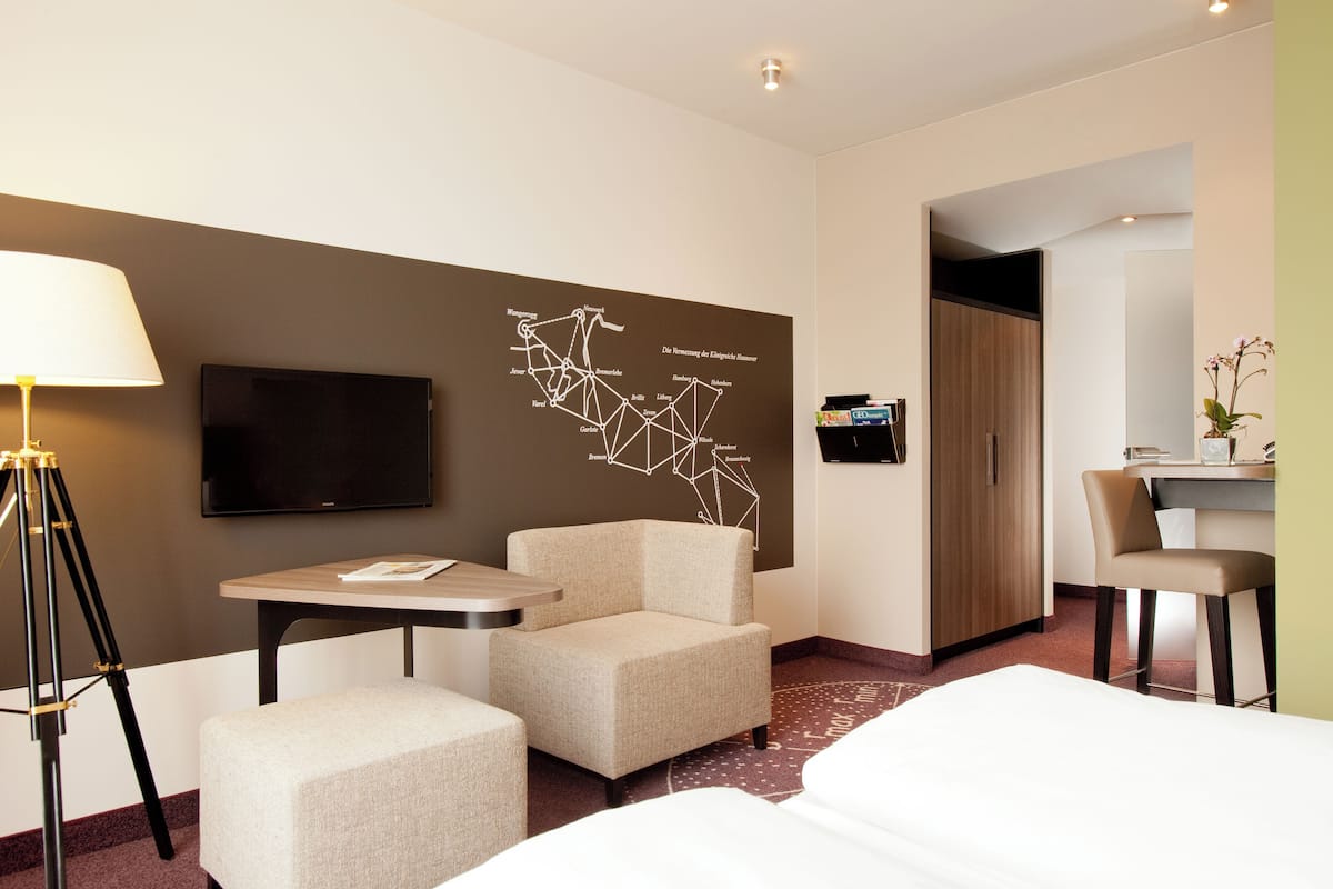 Ein Hotelzimmer mit Bett, Schreibtisch, Stuhl, kleinem Tisch, Lampe und Wandkarte.