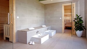 A modern bathroom with a large rectangular sink, two separate sinks, and a wooden sauna door.