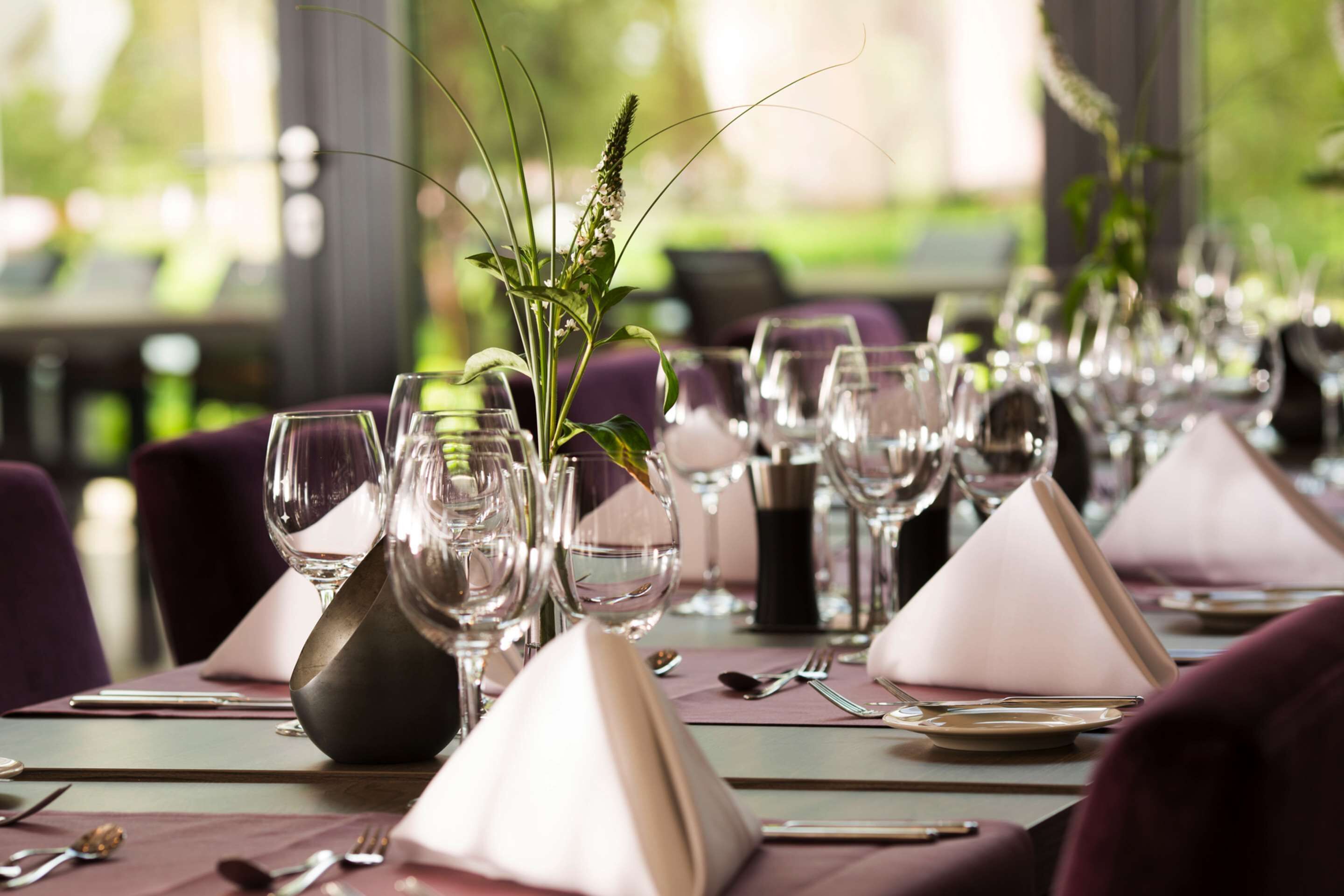 A dining table set with multiple wine glasses, a vase with greenery, and neatly arranged place settings.