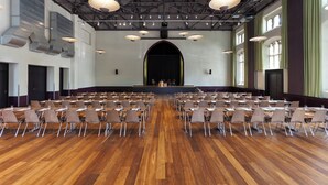 A large hall with rows of chairs facing a stage, equipped with overhead lighting and ventilation.