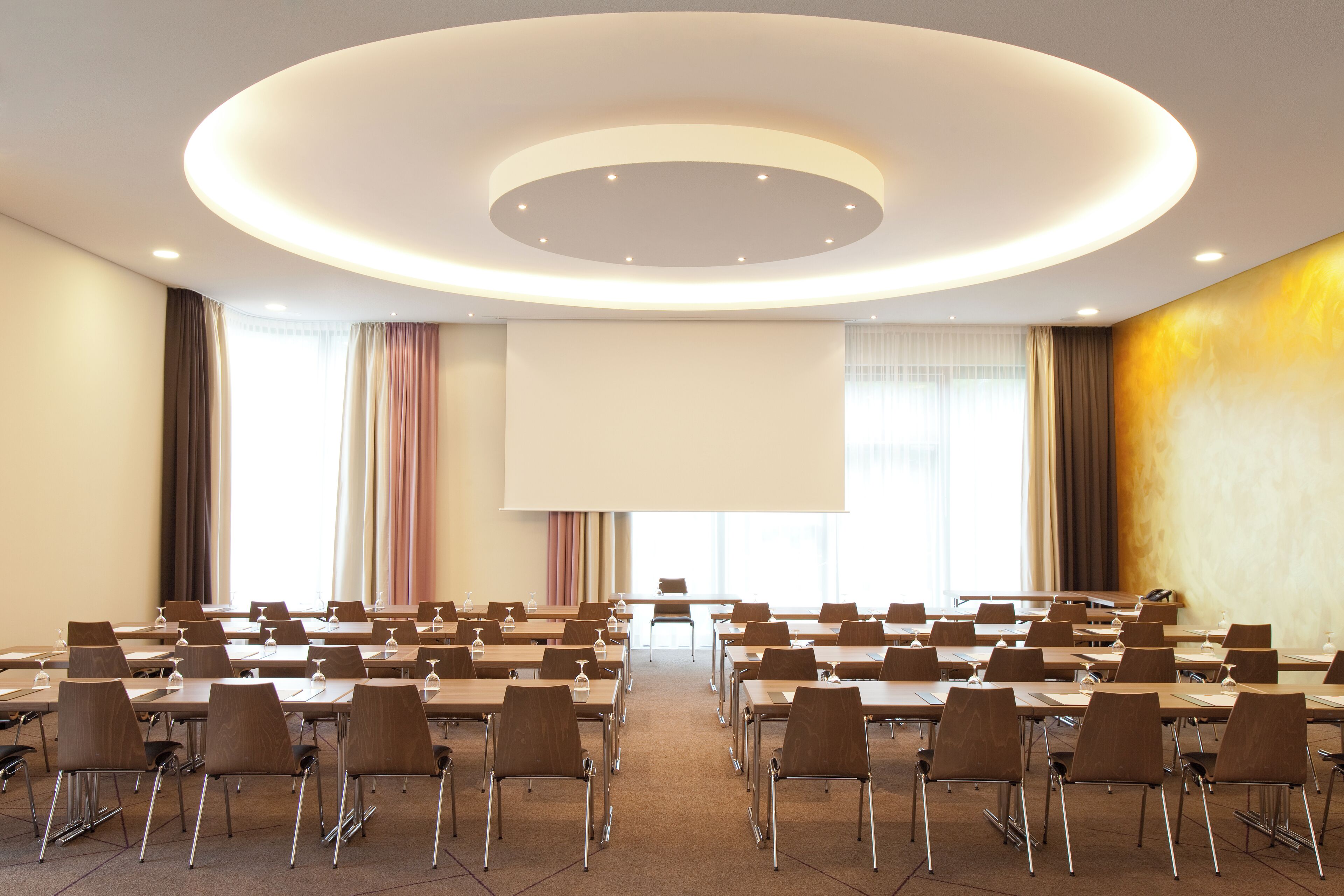 A conference room with a large screen, multiple tables, and chairs arranged for a meeting.