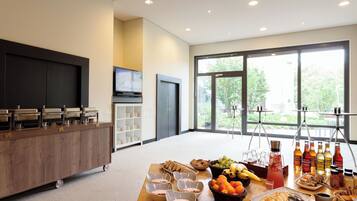 A breakfast buffet with various food items and beverages, a television, and a large window with a view of greenery.