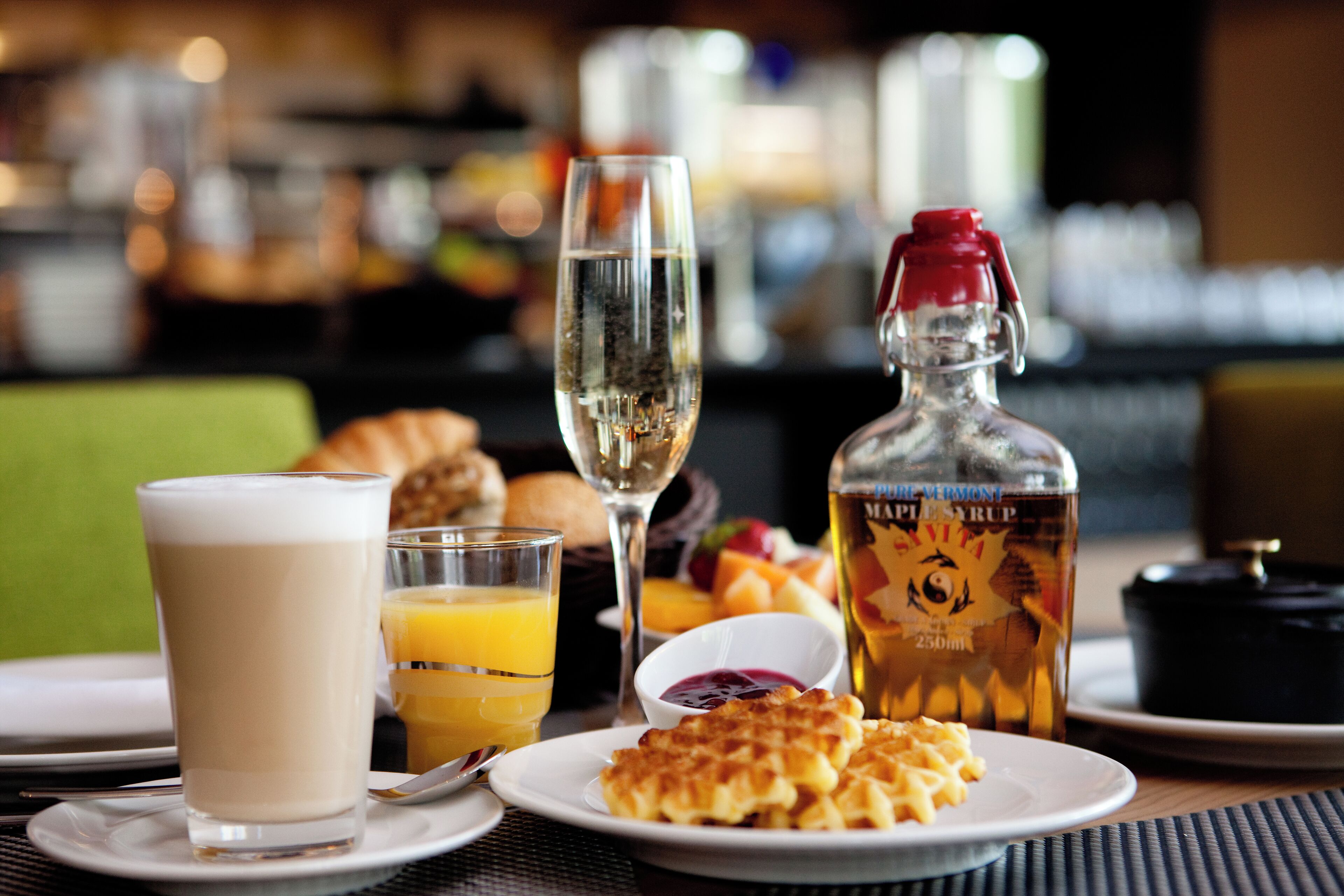 Un desayuno con un vaso de leche, un vaso de jugo de naranja, waffles y una botella de jarabe de arce.