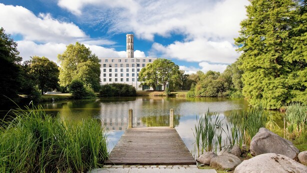 A wooden dock leading to a calm lake with a building in the background.