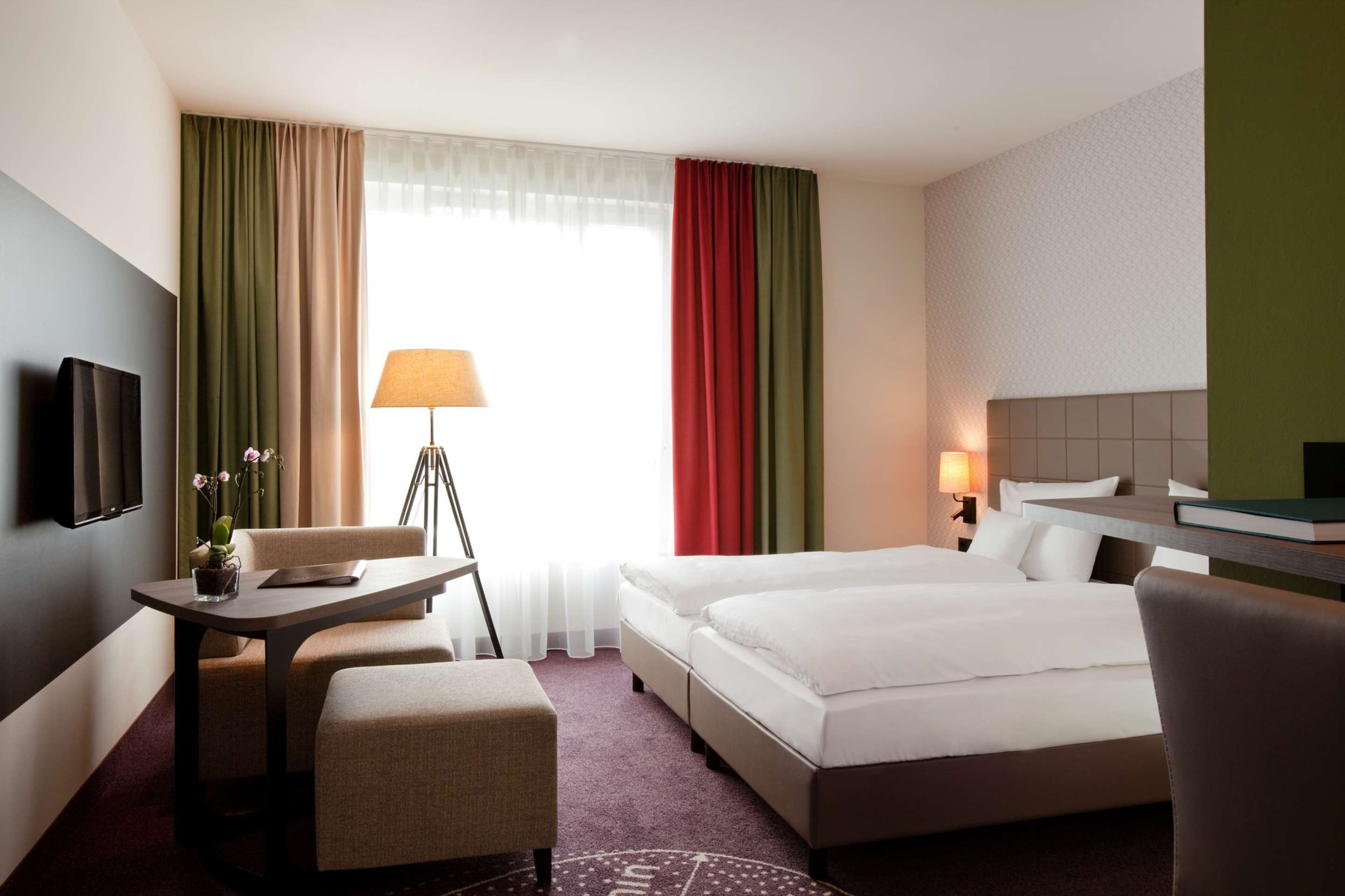 A hotel room with a bed, two chairs, a small table, a lamp, and a TV.