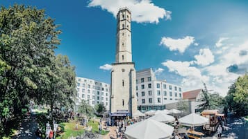 Una torre histórica con un reloj, rodeada de edificios modernos y zonas de estar al aire libre.