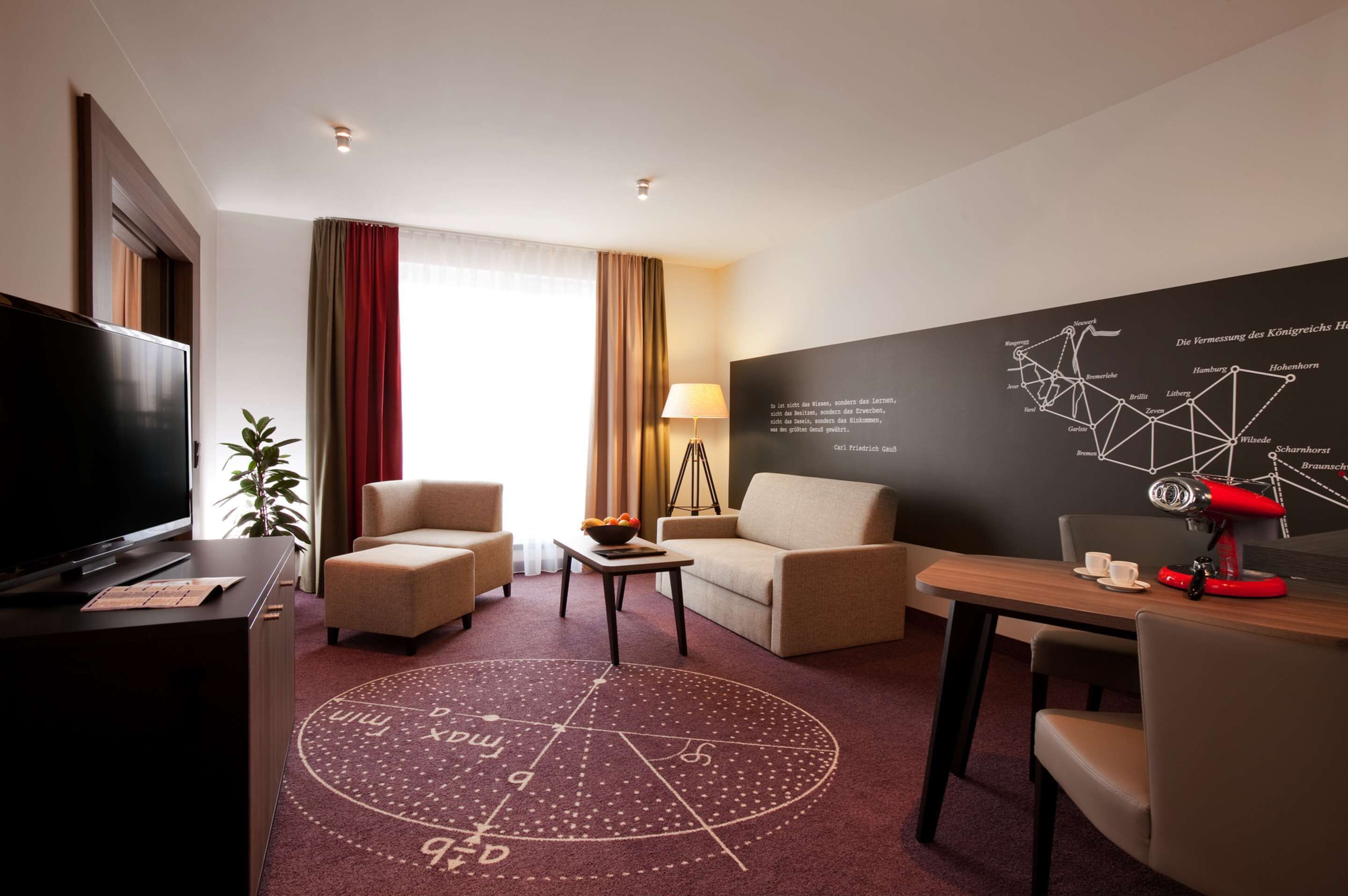 Habitación de hotel con televisor, dos sofás, una mesa de centro, una lámpara y un mapa en la pared.