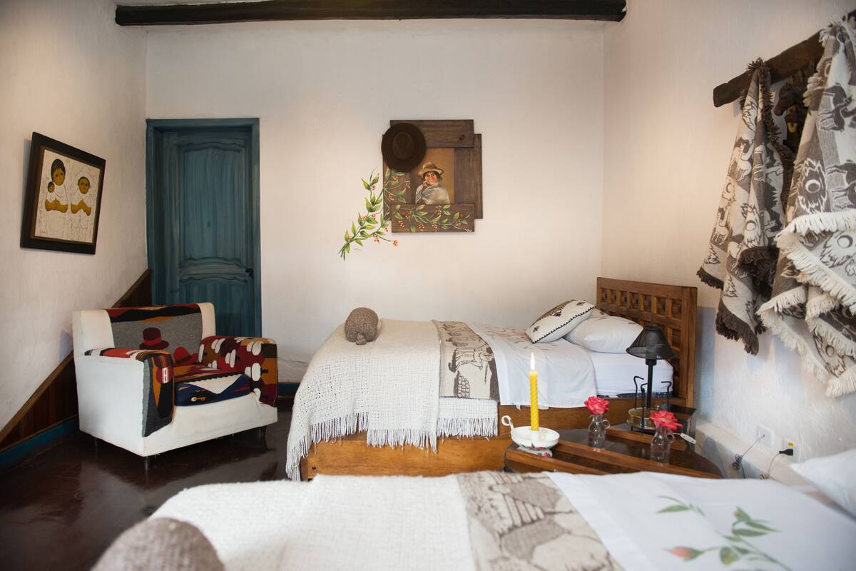 A cozy bedroom with a wooden bed, a blue door, a framed picture, and a small table with a candle.