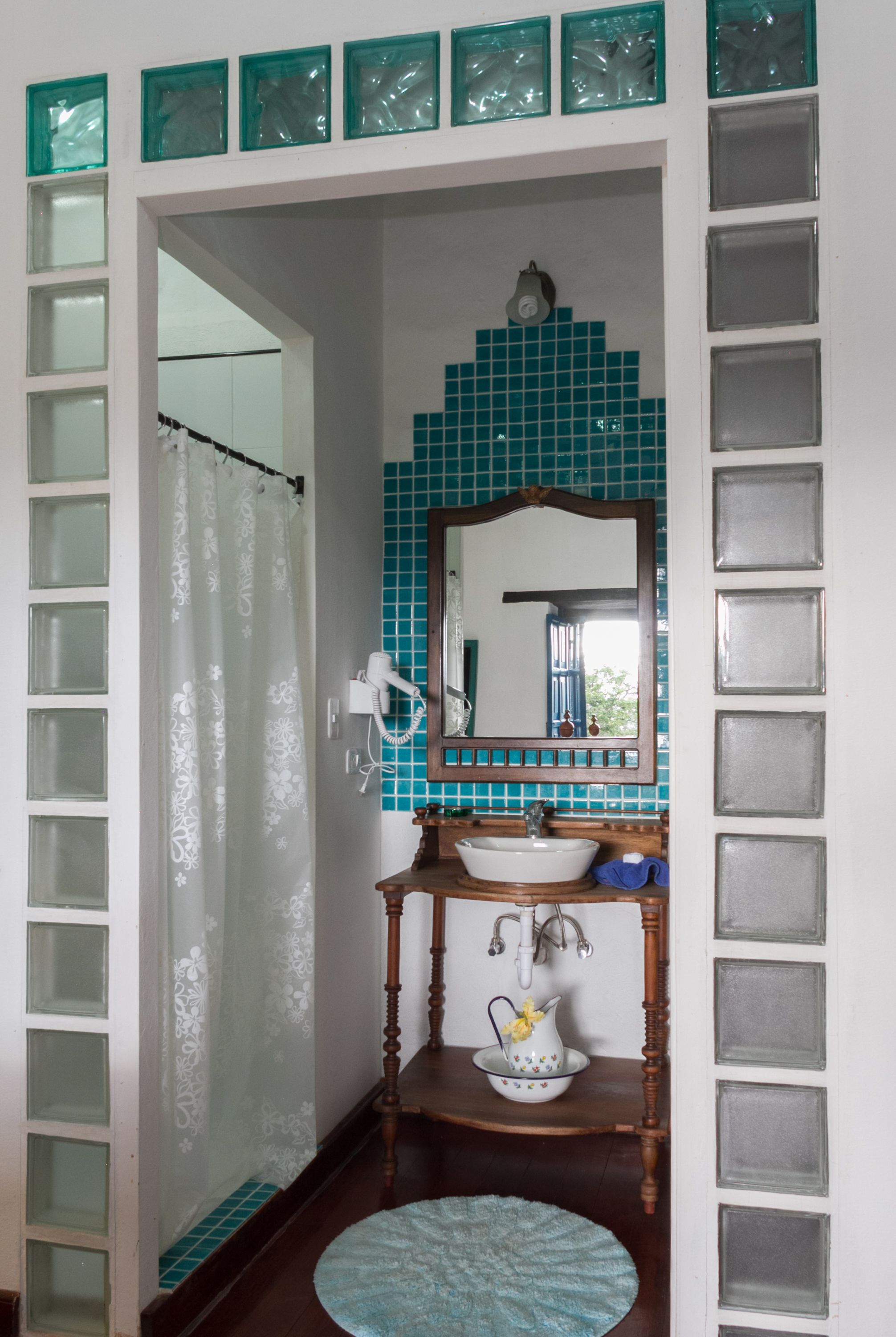 Un baño con ducha, lavabo y espejo, y una alfombra azul.