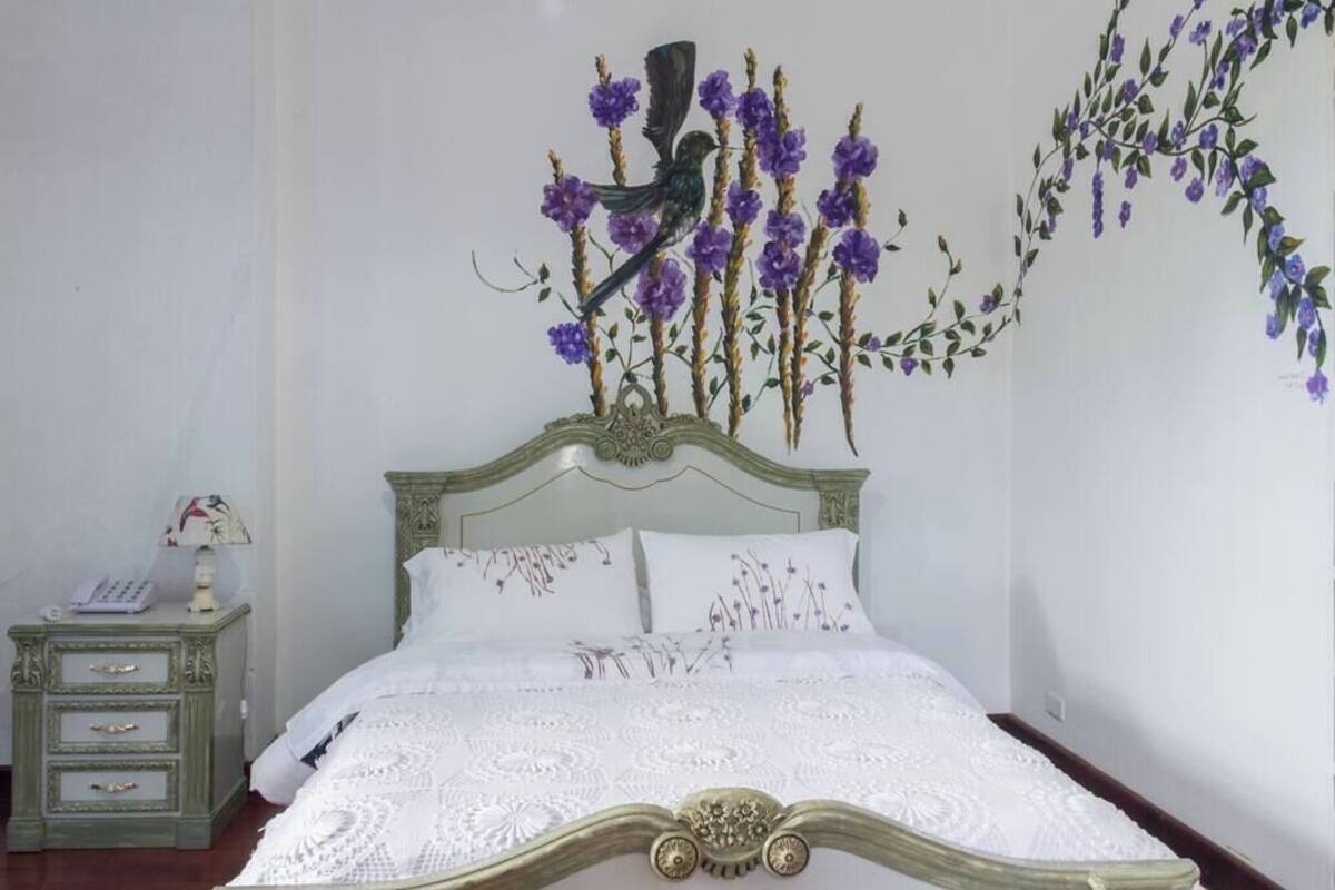 A bedroom with a bed, a nightstand, and a wall decoration of a bird and flowers.