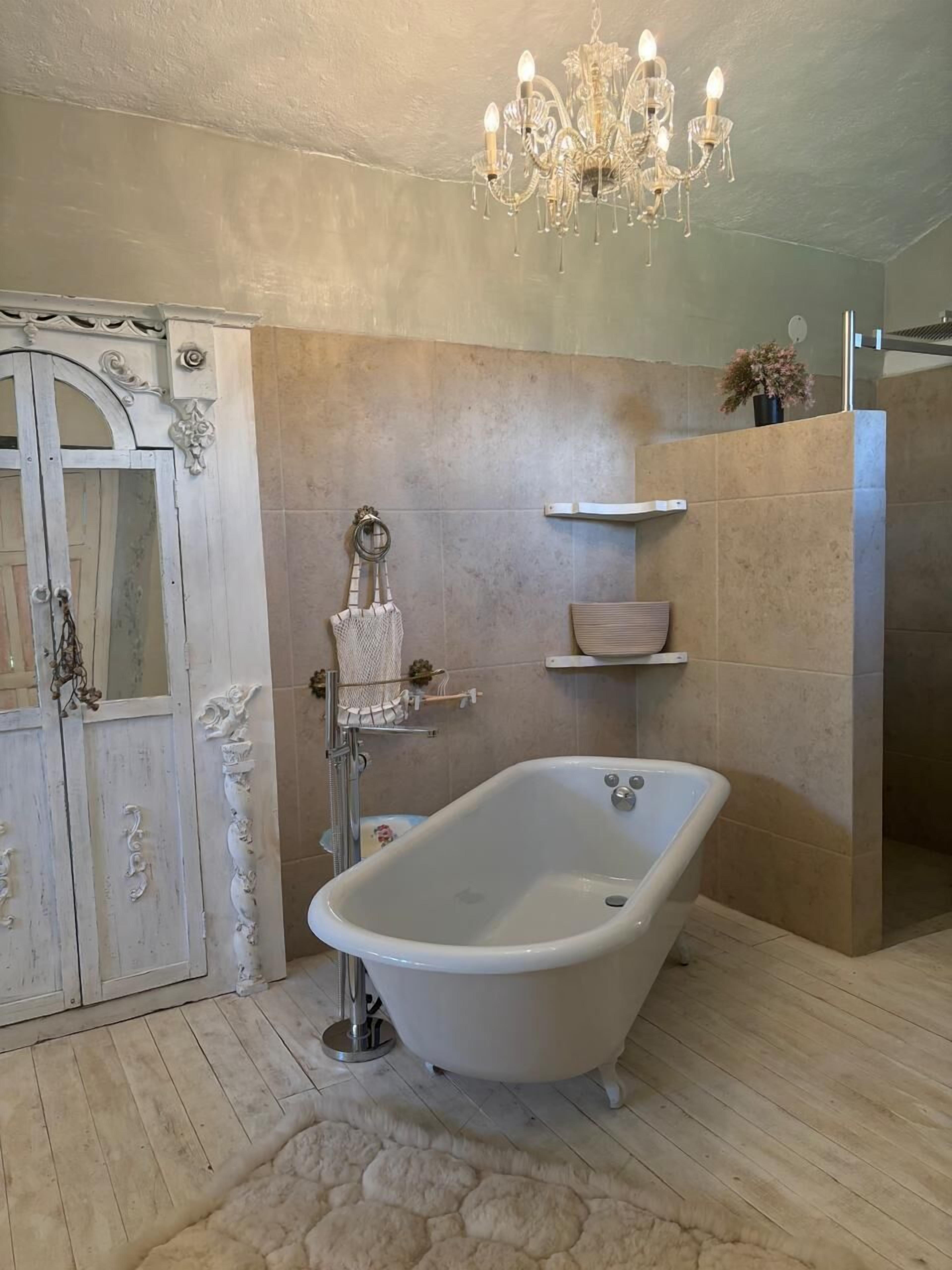Un baño con una bañera independiente, una araña, un perchero para toallas y un espejo decorativo.