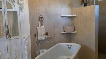 Un baño con una bañera independiente, una araña, un perchero para toallas y un espejo decorativo.