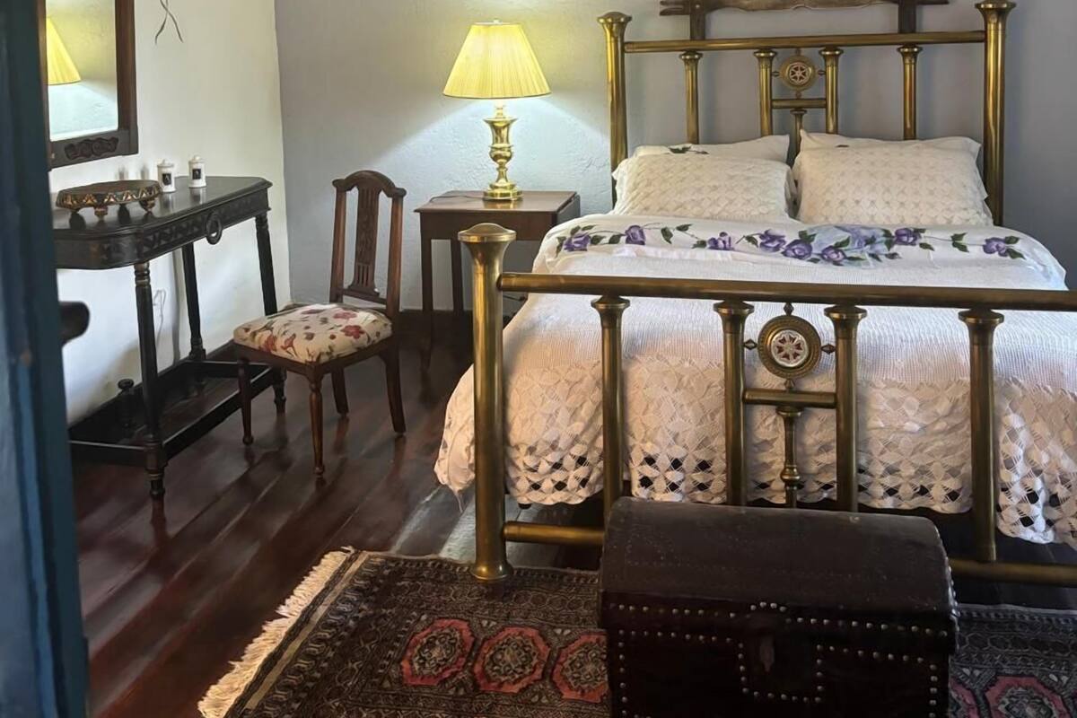 A bedroom with a bed, a nightstand, a lamp, a chair, a mirror, and a painting.