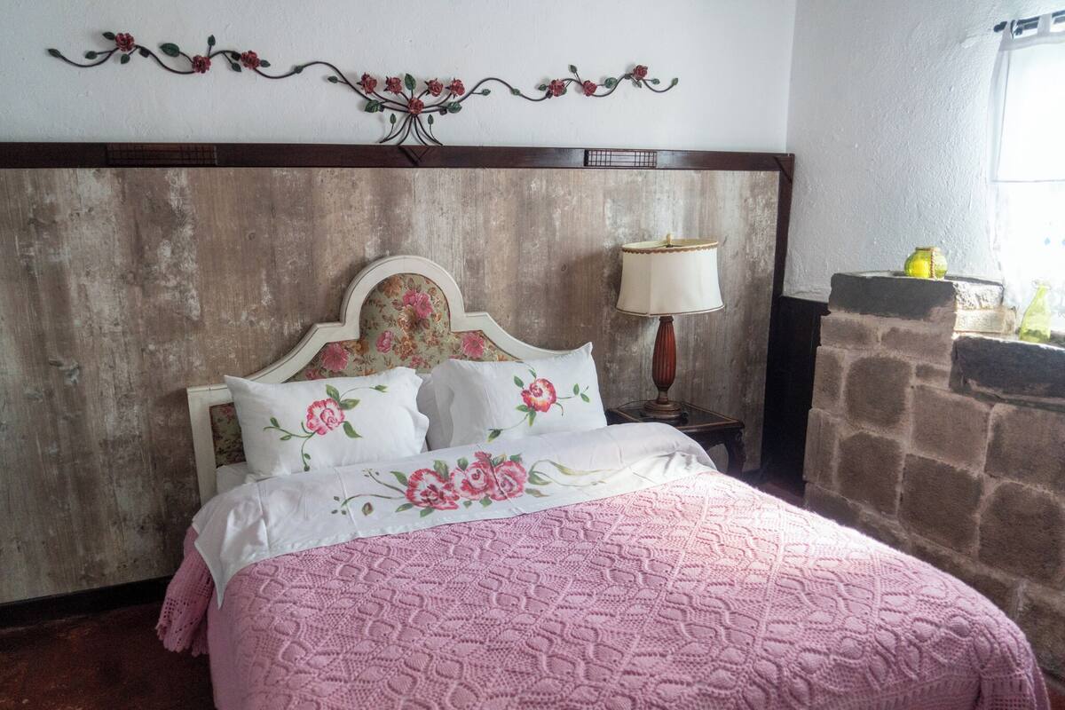 A bedroom with a wooden headboard, floral bedspread, and a nightstand with a lamp.