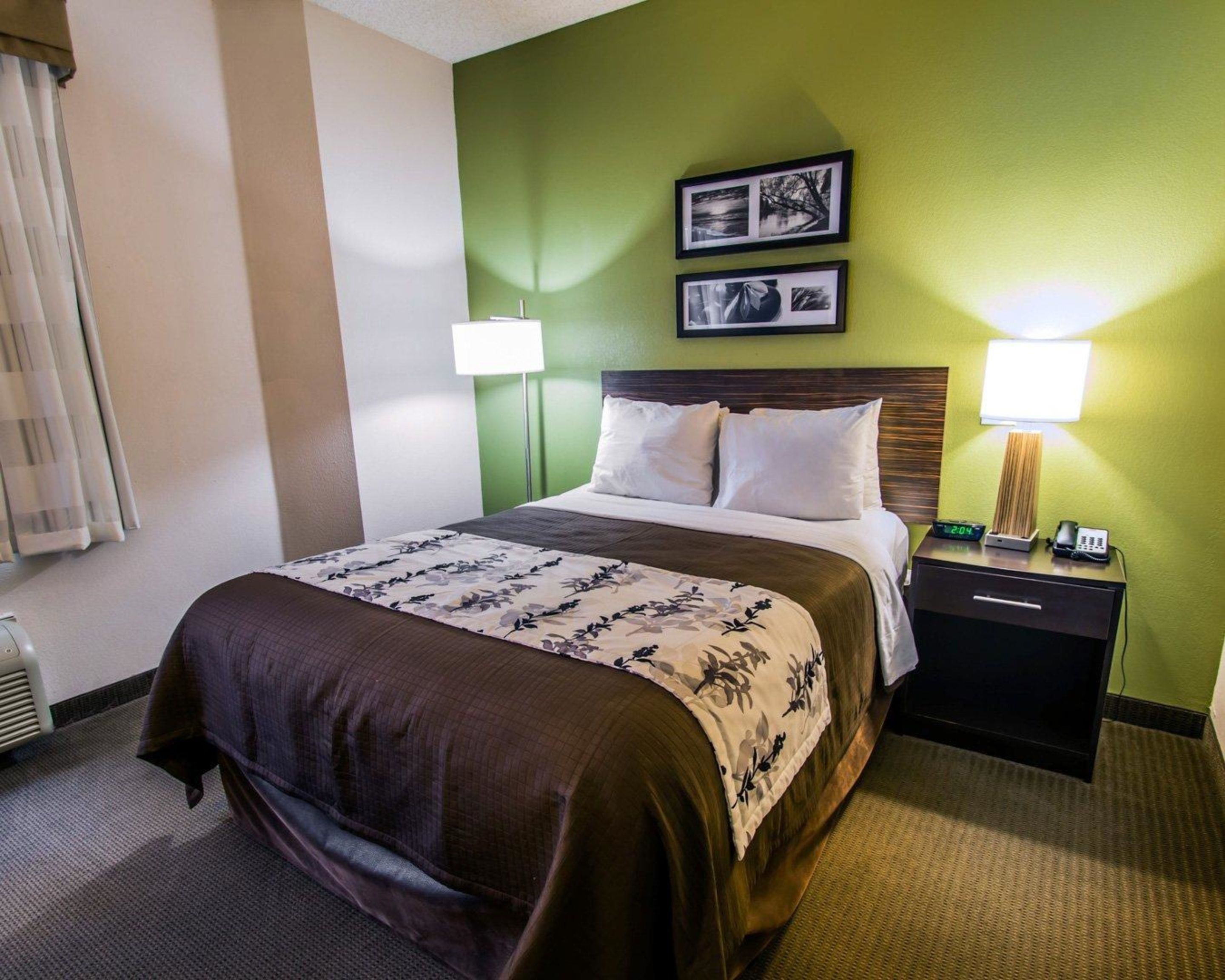 A hotel room with a bed, two bedside lamps, a nightstand with a phone and a lamp, and two framed pictures on the wall.